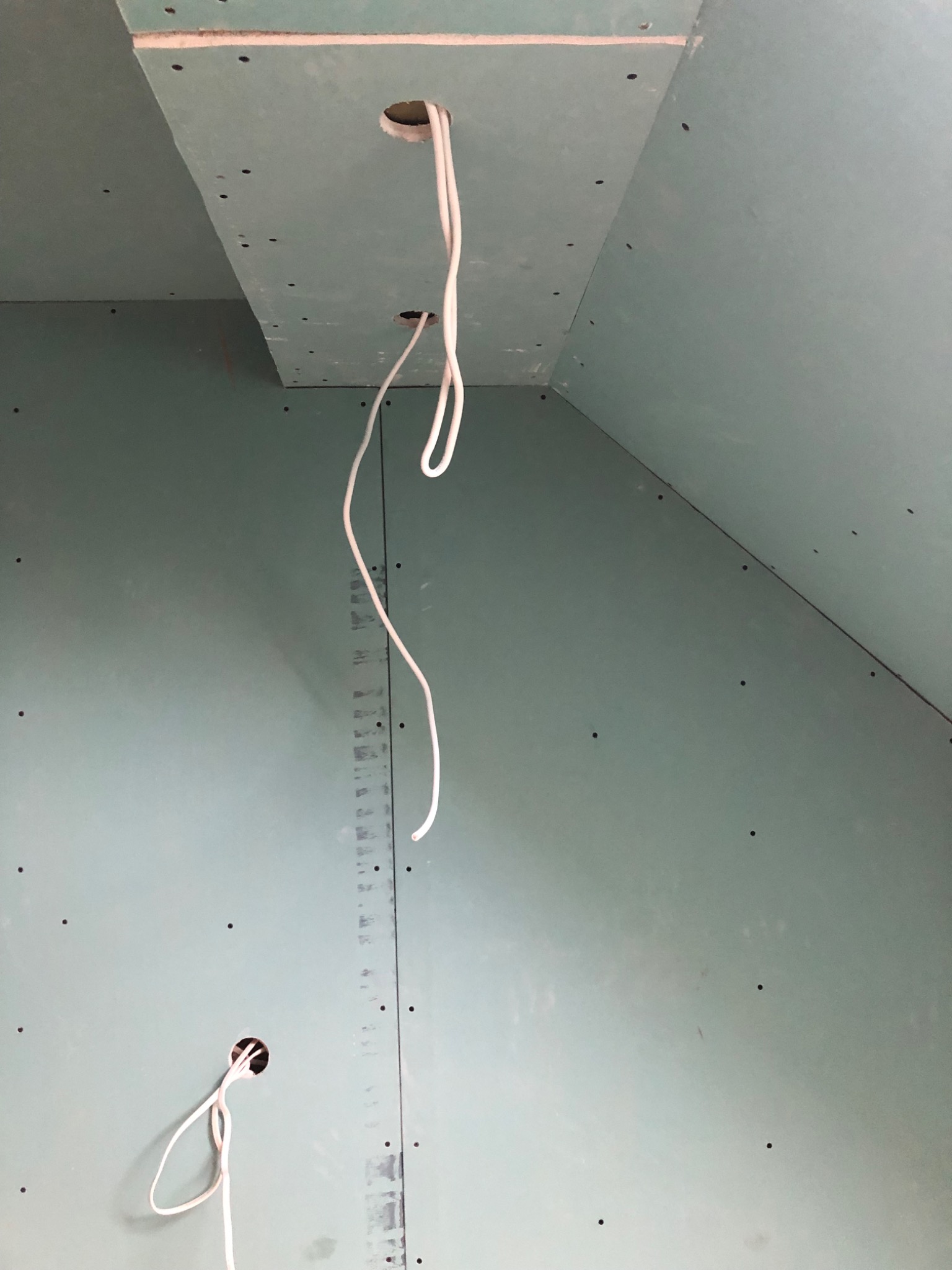 Ściana i sufit pokryte zielonymi płytami gipsowo-kartonowymi z widocznymi otworami na kable elektryczne, w trakcie montażu.