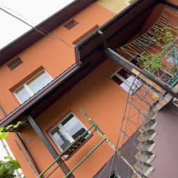 Usługi ogólnobudowlane - Pomarańczowo-żółta elewacja domu po remoncie, widok z dołu, z elementami rusztowania i dekoracyjną balustradą balkonu. Ukończone tynkowanie elewacji.