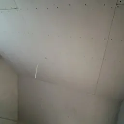 Poddasze z zamontowanymi płytami kartonowo-gipsowymi, widoczne ślady po wkrętach, fragment drabiny, oświetlenie robocze.