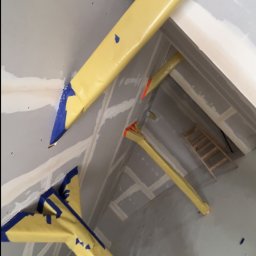 Usługi ogólnobudowlane - Skośne ujęcie fragmentu wnętrza w trakcie prac wykończeniowych; widoczne profile zabezpieczone folią i płyty kartonowo-gipsowe na ścianach.