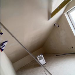 Usługi ogólnobudowlane - Poddasze po nałożeniu gładzi, widoczne narzędzia i poziomica. Ściany i sufit w jasnym odcieniu, przygotowane do dalszych prac wykończeniowych.