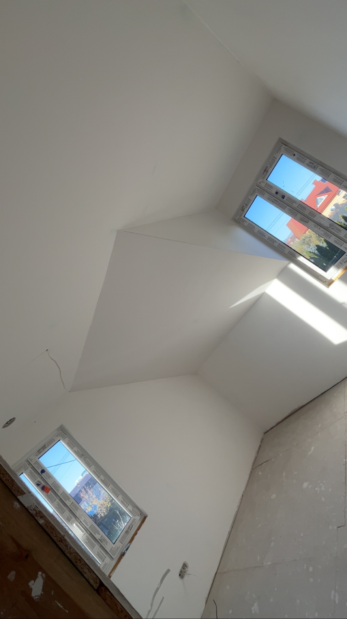 Białe poddasze po remoncie: skośny sufit z oknami dachowymi, ściany przygotowane do malowania. Widoczne gniazdka elektryczne i fragment drewnianej konstrukcji.