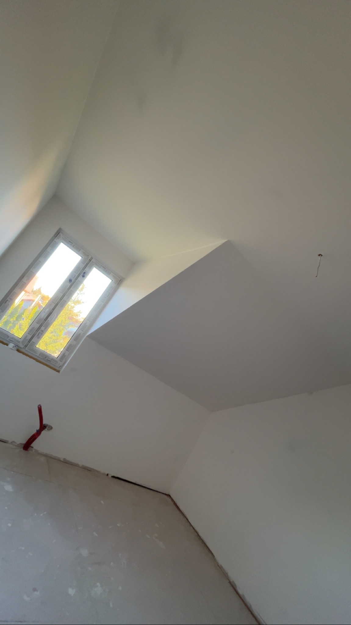 Poddasze po remoncie: gładkie, białe ściany, okno dachowe wpuszczające światło, widoczne instalacje. Świeżo wykończone wnętrze z ukośnym sufitem.