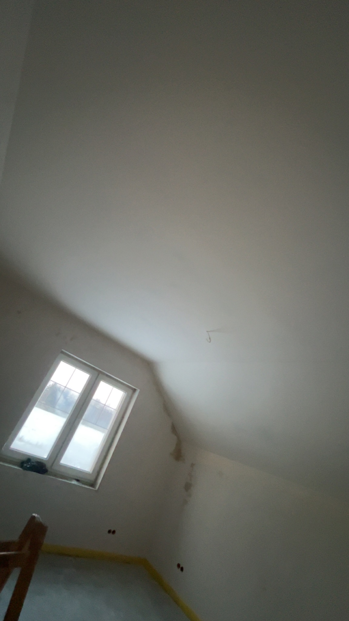 Poddasze po gładziowaniu, widoczne okno dachowe, ściany przygotowane do malowania. Na podłodze folia zabezpieczająca. Widoczne ślady po zalaniach.