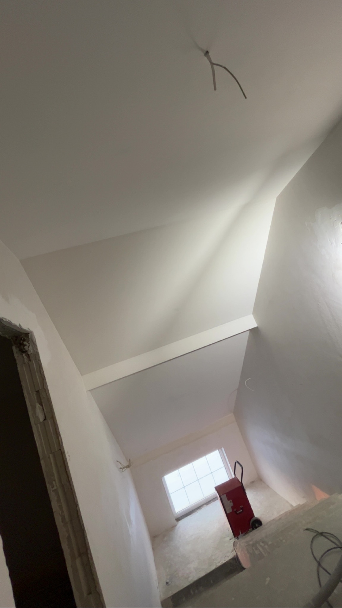 Wnętrze po gładziowaniu w Zawistach Podleśnych: białe ściany i sufit, widoczne kable, czerwony agregat szpachlarski. Świeżo wykończone pomieszczenie.