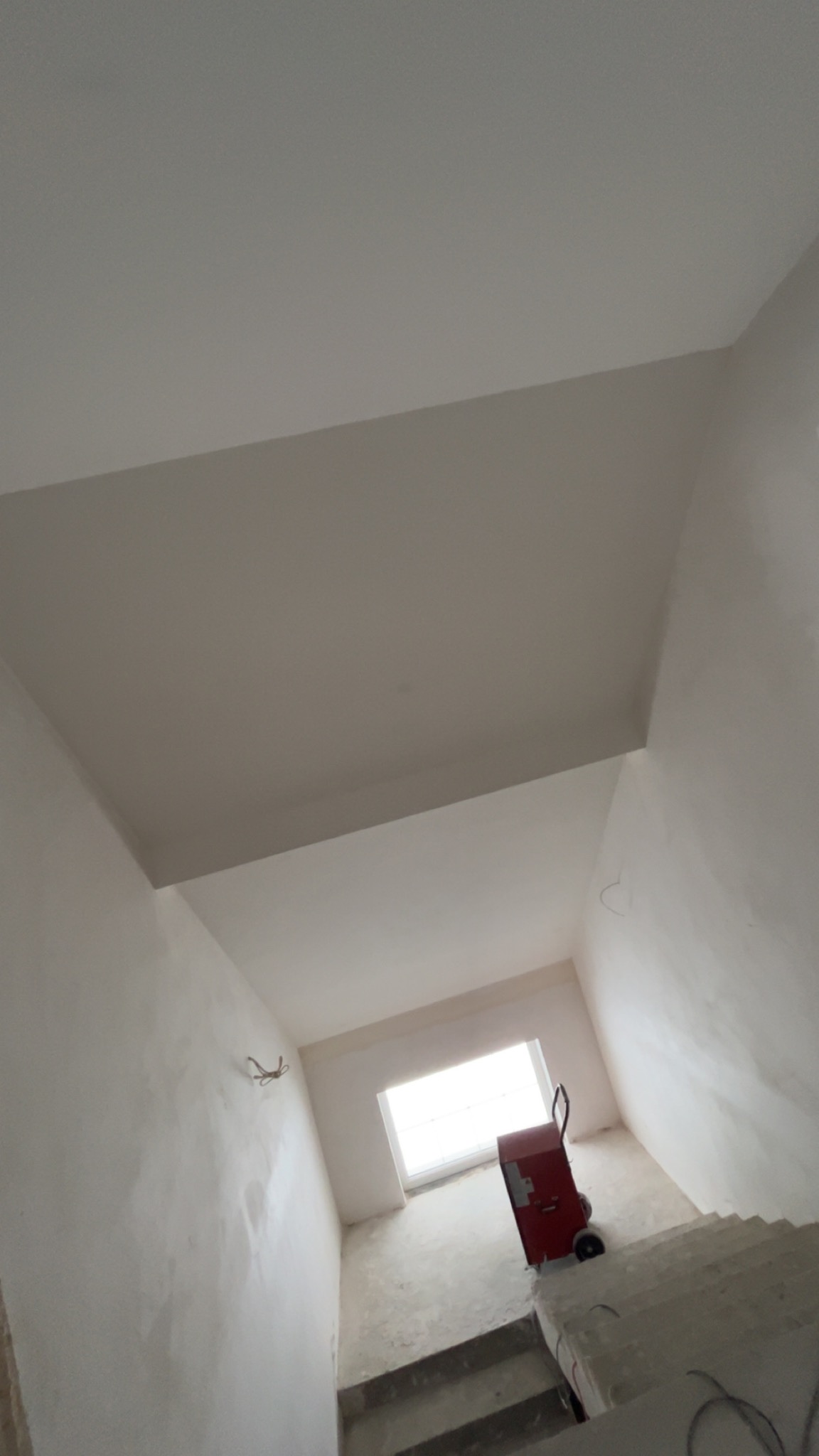 Wnętrze klatki schodowej po gładziowaniu ścian i sufitu, widoczny wózek malarski i schody. Świeżo wykończone powierzchnie w jasnym odcieniu bieli.