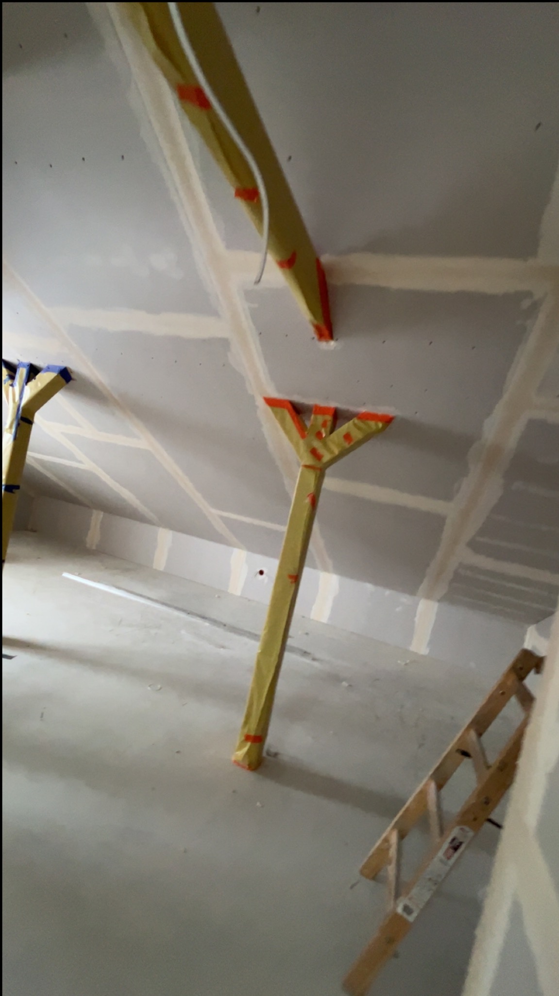 Poddasze w trakcie wykańczania: widoczne płyty gipsowe na skosach, drewniane podpory zabezpieczone folią, drabina. Prace wykończeniowe w surowym wnętrzu.