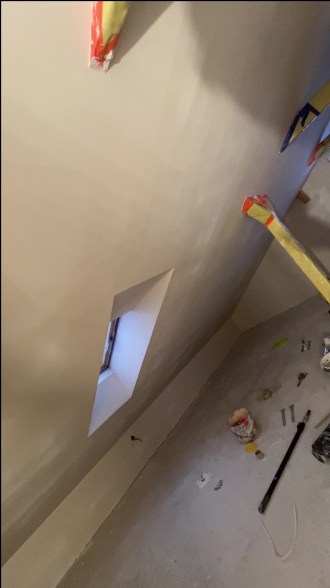 Wnętrze po gładziowaniu ścian i sufitu, widoczne okno w skosie, narzędzia malarskie na podłodze. Ściany w jasnym odcieniu beżu, gotowe do malowania.