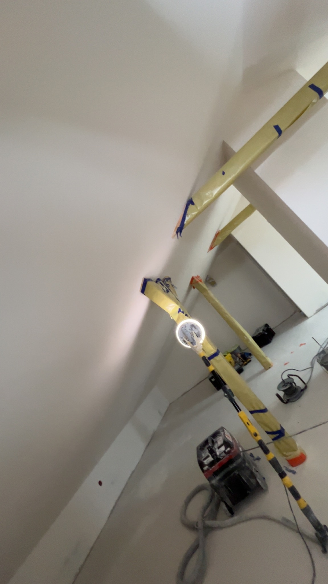 Poddasze po nałożeniu gładzi, widoczna szlifierka teleskopowa z oświetleniem, przygotowane elementy konstrukcyjne. Praca w toku, widok z dołu, oświetlenie robocze.