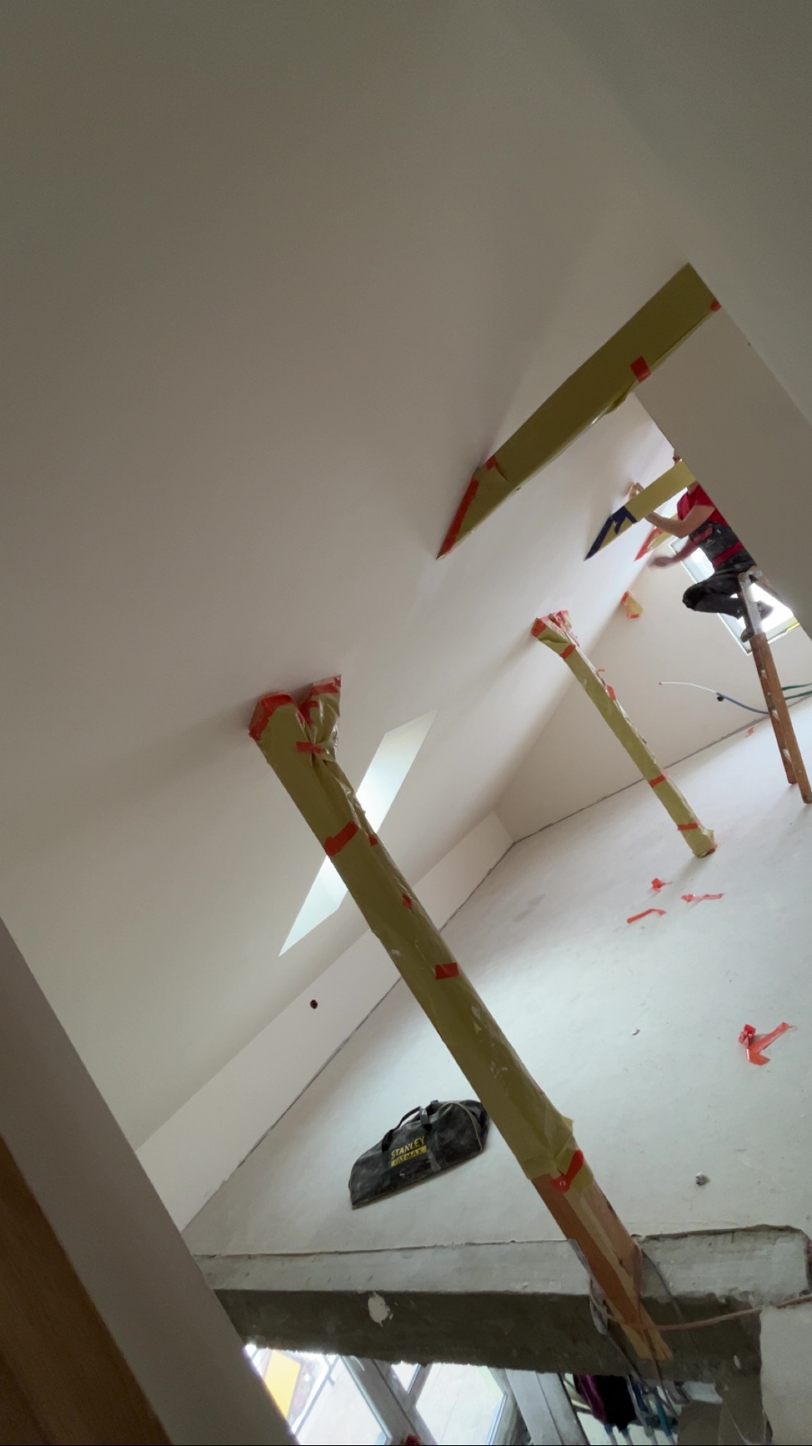 Skośny sufit poddasza z oknami dachowymi w trakcie wygładzania. Widoczne rusztowanie i narzędzia pracy. Praca na wysokości.