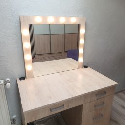 ARMAR MEBLE - Toaletka z jasnego drewna z lustrem otoczonym żarówkami, odbijająca szafę przesuwną i fioletowy puf.