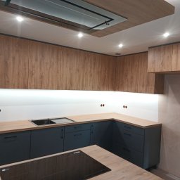 ARMAR MEBLE - Nowoczesna kuchnia na wymiar w Aleksandrowie Kujawskim z drewnianymi górnymi szafkami i grafitowymi dolnymi, oświetleniem LED pod szafkami i czarną płytą indukcyjną na wyspie.