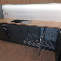 ARMAR MEBLE - Szare szafki kuchenne z drewnianym blatem, wysuwany kosz cargo na naczynia i otwartą zmywarką po lewej stronie.