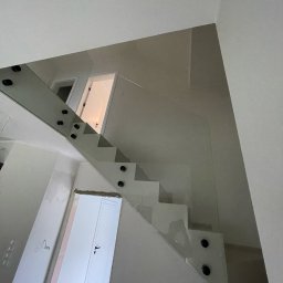 HomeGlass - Wewnętrzne schody z balustradą ze szkła hartowanego, mocowaną punktowo, widok z dołu, z widocznymi drzwiami na obu poziomach.