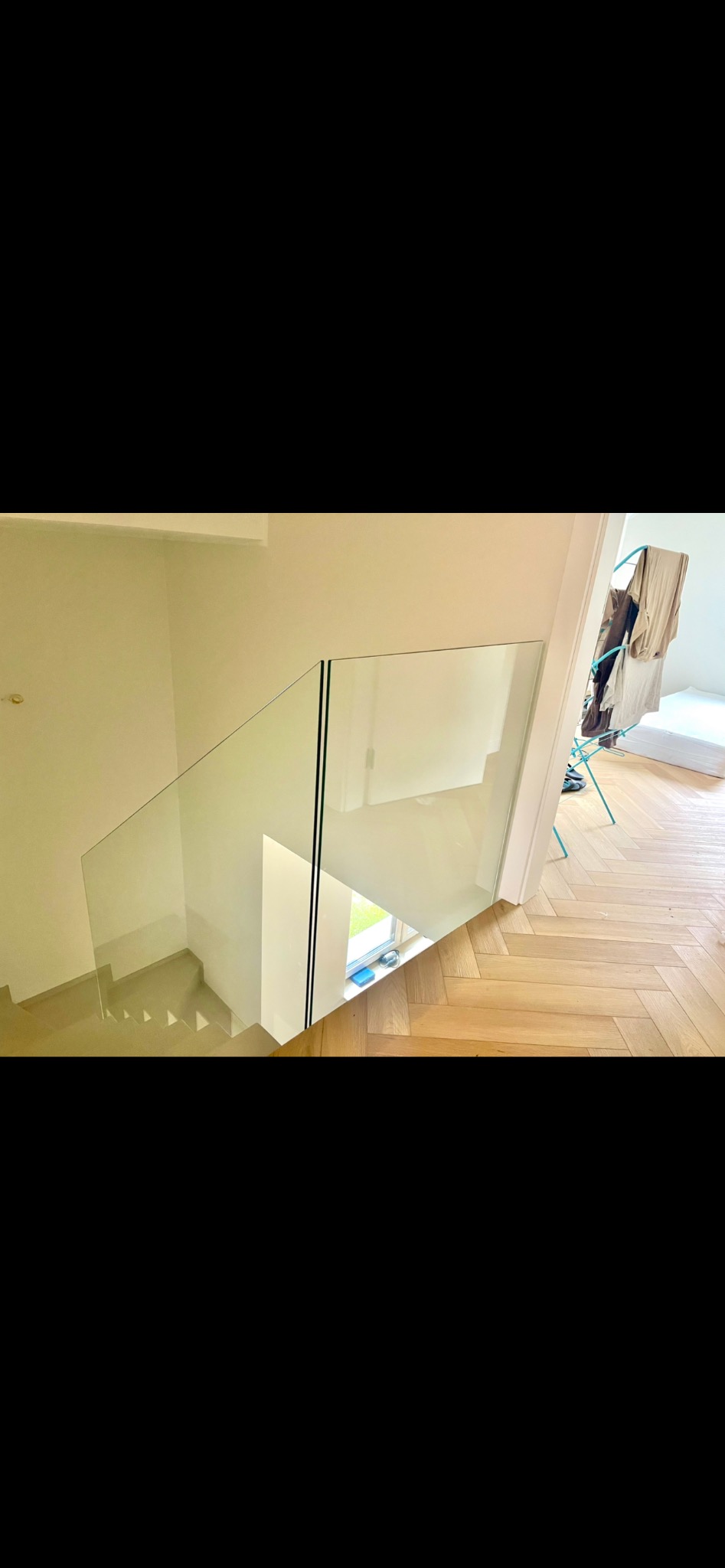 Szklana balustrada na schodach wewnętrznych z drewnianymi stopniami i parkietem w jodełkę, widok z góry, w tle suszarka na pranie.