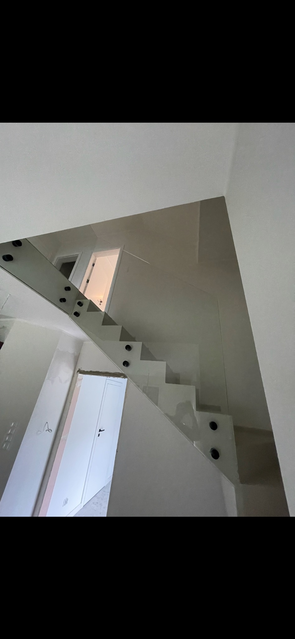 Wewnętrzne schody z balustradą ze szkła hartowanego, mocowaną punktowo, widok z dołu, z widocznymi drzwiami na obu poziomach.