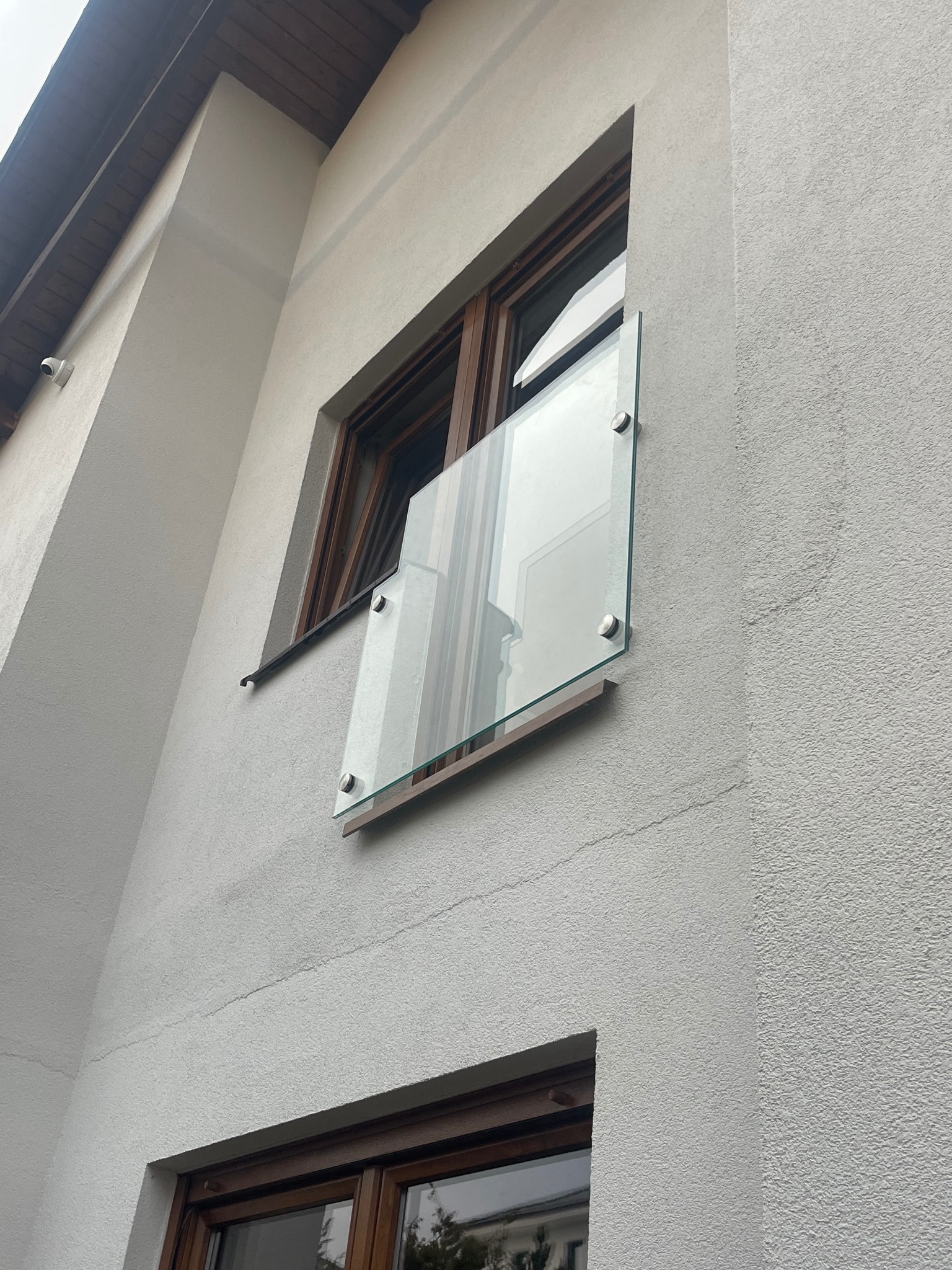 Szklana balustrada balkonowa zamontowana na elewacji budynku z drewnianą ramą okienną, widoczna z dołu pod kątem.