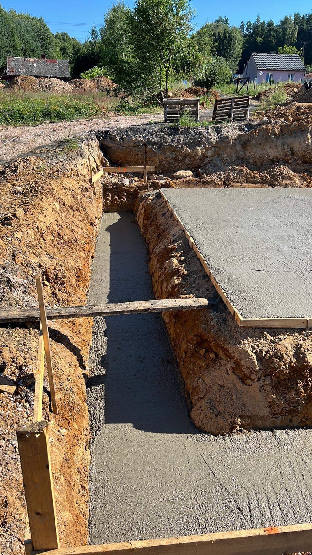 Wylana betonowa podstawa fundamentu w wykopie, z widocznym deskowaniem i drewnianymi podporami, teren budowy.
