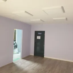 Wnętrze biura po malowaniu, ściany w odcieniach fioletu, drewnopodobna podłoga, białe panele sufitowe i czarne drzwi z napisem 'BIURO'.