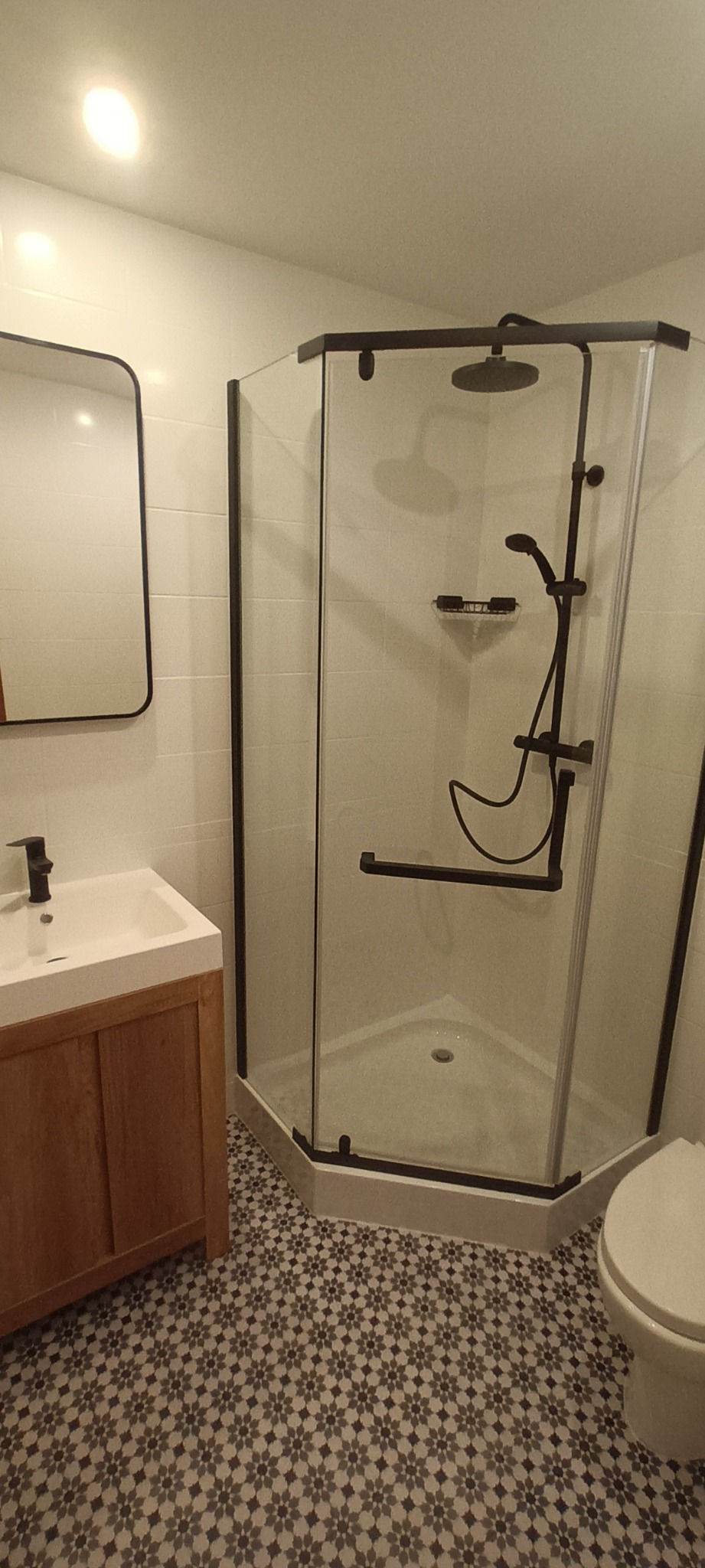 Nowoczesna łazienka z kabiną prysznicową z czarnymi ramami, umywalką z drewnianą szafką i wzorzystą podłogą.