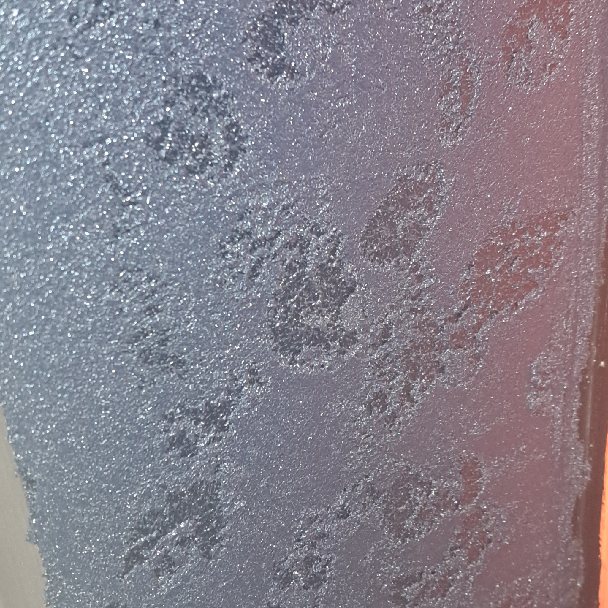 Szara, chropowata powierzchnia z efektem dekoracyjnym przypominającym gładź strukturalną, z widocznymi nieregularnymi wzorami i refleksami światła, częściowo oświetlona od prawej strony.