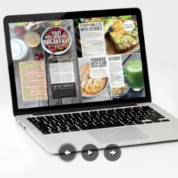 Laptop wyświetla artykuł o przepisach na śniadania po treningu, prezentując zdjęcia potraw i listę zakupów, na białym tle.