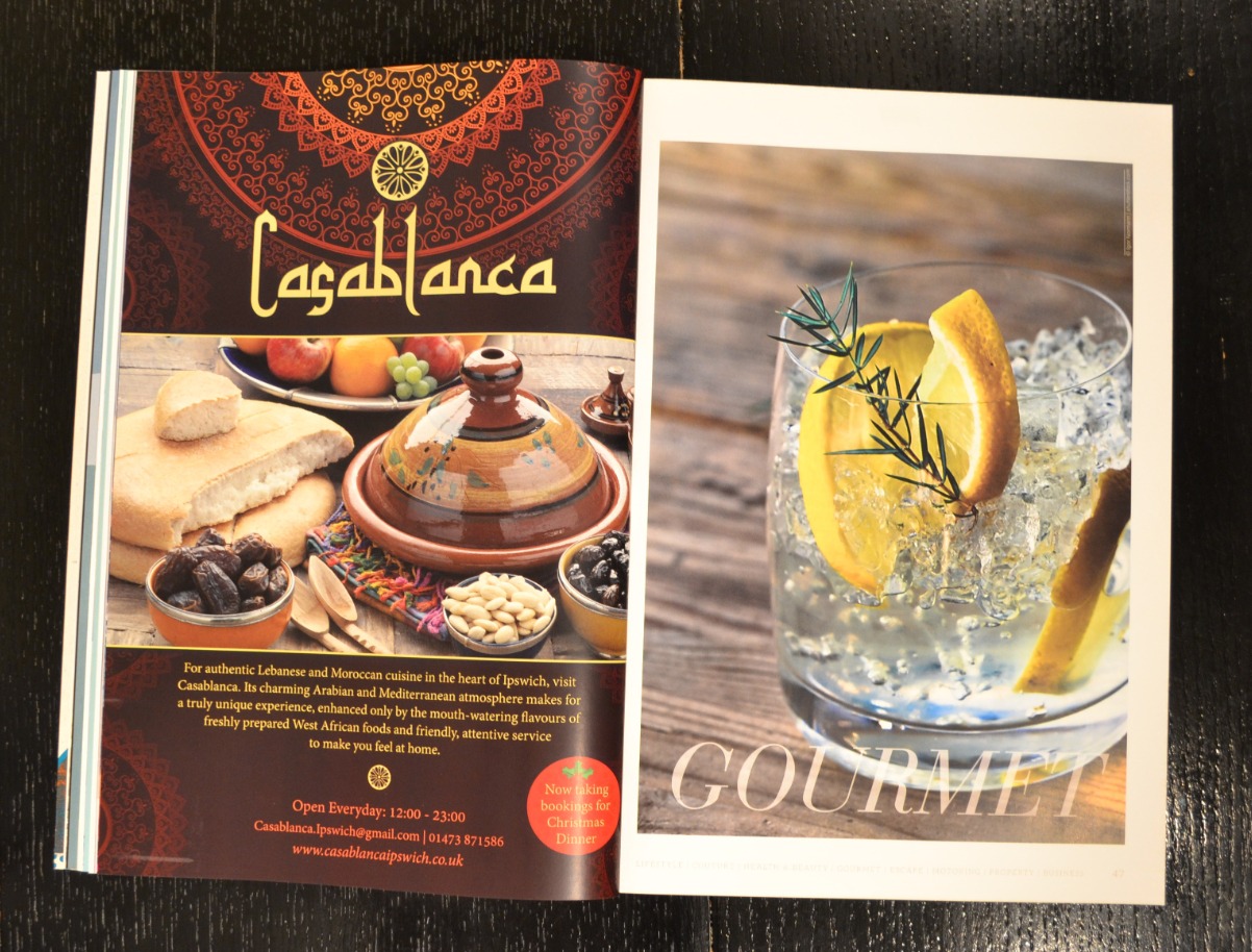 Otwarta gazeta z reklamą restauracji Casablanca i zdjęciem drinka z cytryną i lodem, na ciemnym drewnianym tle.