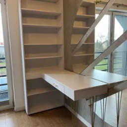 Białe biurko z regałem połączone z toaletką z owalnym lustrem w metalowej ramie, wsparte na złotych n&oacute;żkach w jasnym pokoju.