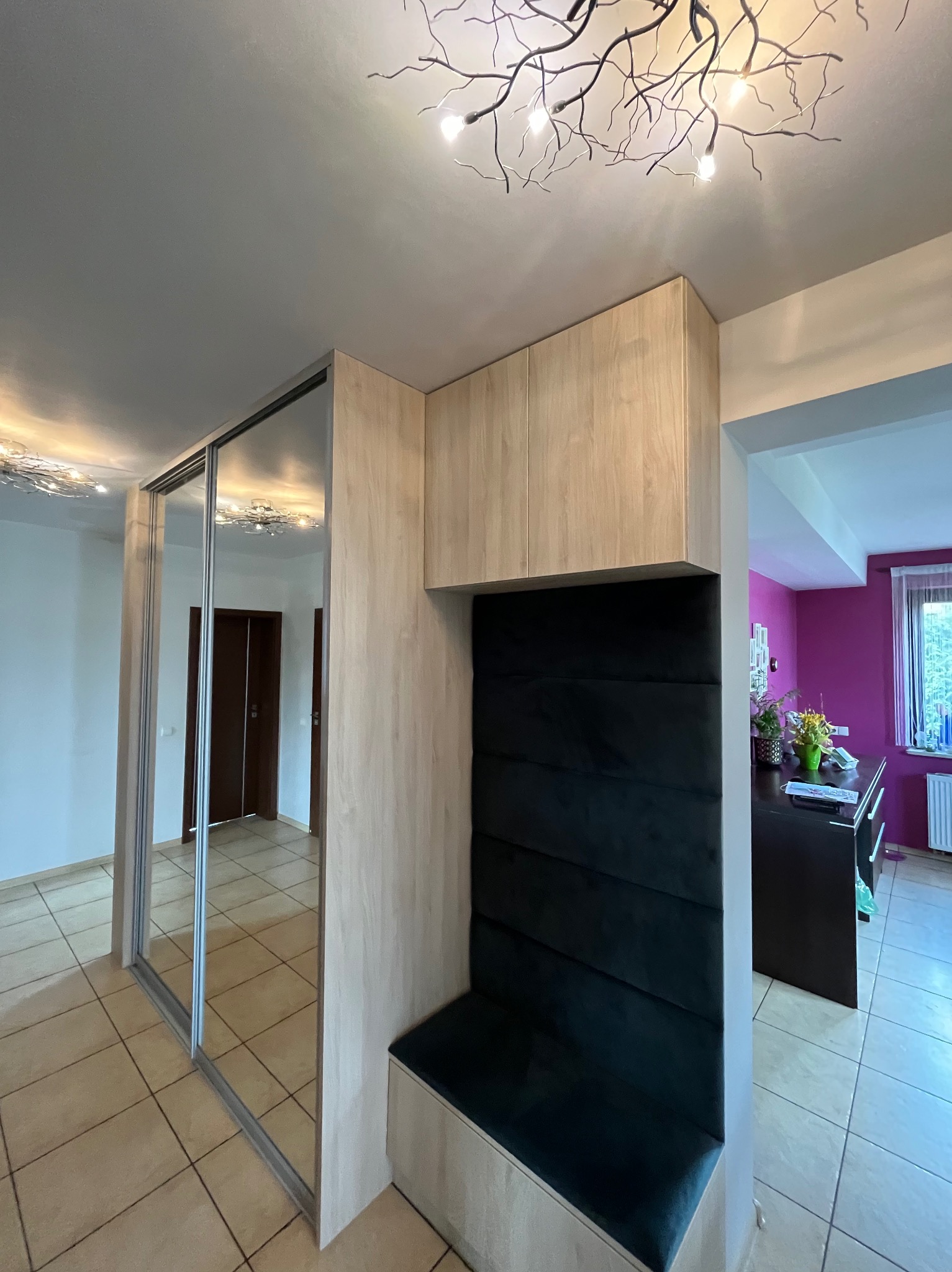 Szafa wnękowa z lustrzanymi drzwiami przesuwnymi i siedziskiem z ciemną tapicerką, oświetlenie sufitowe w kształcie gałęzi, widok na fuksjowy pokój.