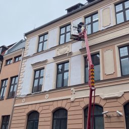 MALAR STUDIO - Pracownik na podnośniku koszowym podczas renowacji elewacji kamienicy, widoczne fragmenty odnowionej i przygotowanej do odnowienia powierzchni.