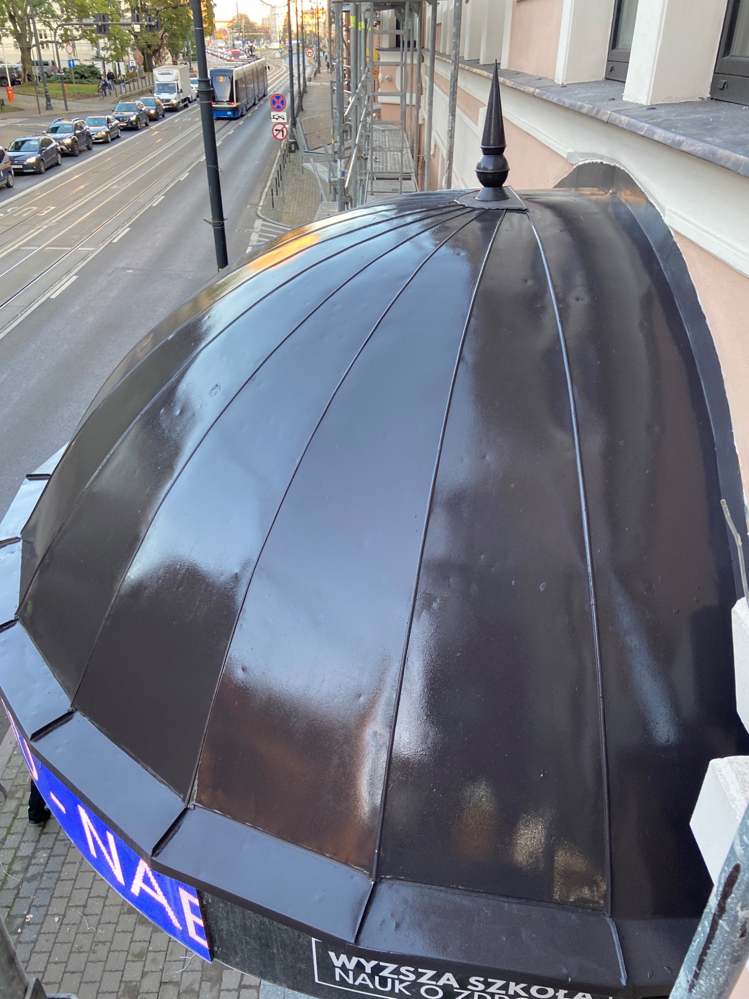 Kopuła budynku pomalowana na czarno, widok z góry na ulicę z tramwajem i rusztowania.