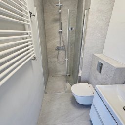 Michał Winiarski - Nowoczesna łazienka w odcieniach szarości z kabiną prysznicową, wiszącą toaletą i grzejnikiem drabinkowym. Minimalistyczny design z akcentami chromu.