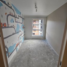 Michał Winiarski - Pokój po remoncie z tapetą w motywy drogowe i pojazdów. Ściana pomalowana na szaro. Podłoga surowa, przygotowana do dalszych prac. Widok z perspektywy drzwi.