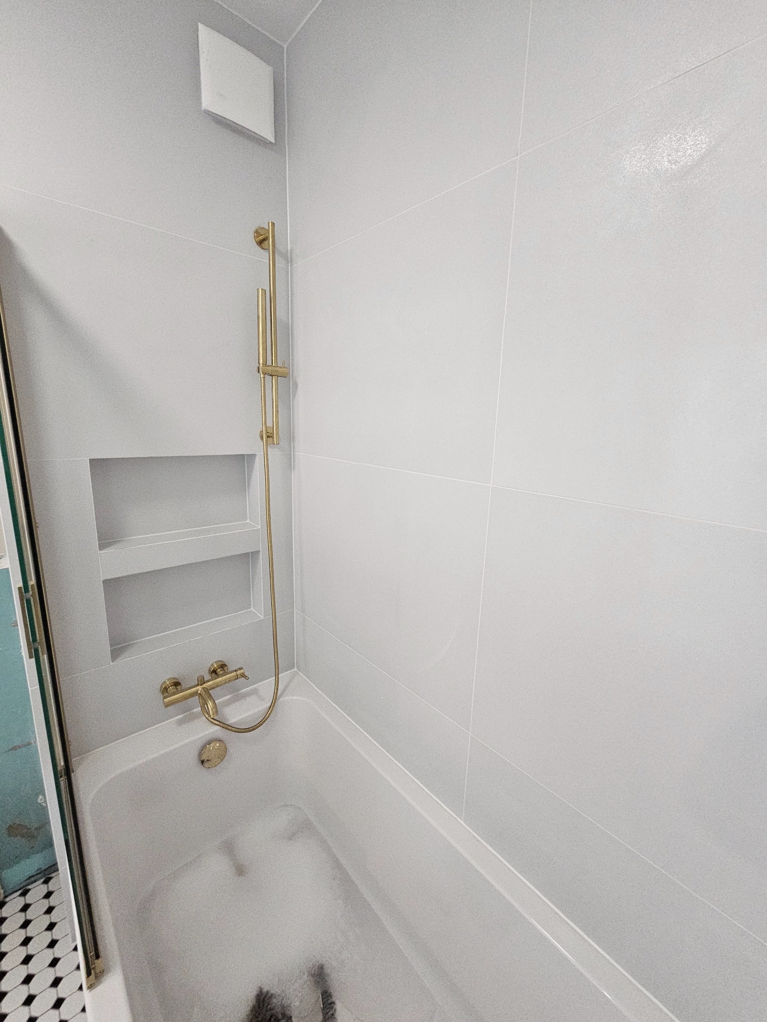 Biała łazienka z wanną wypełnioną pianą, złota armatura, wnęka w ścianie wyłożonej płytkami. Minimalistyczny design, czyste linie, nowoczesne wykończenie.