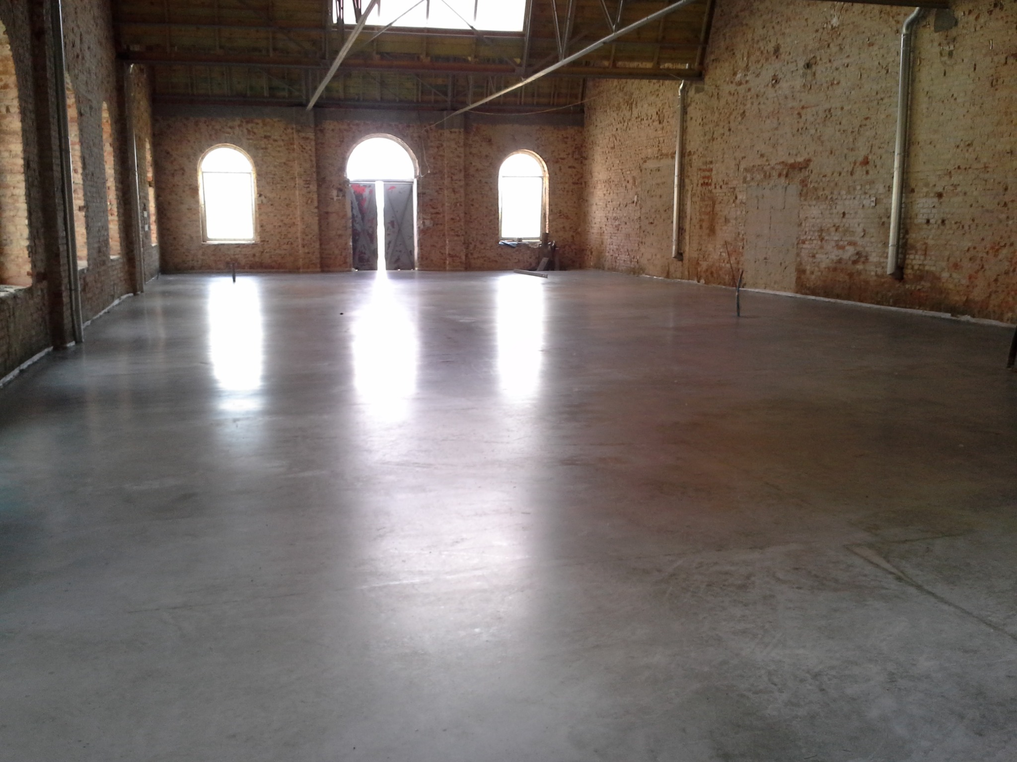 Gładka, szara powierzchnia w hali z ceglanymi ścianami i łukowymi oknami, refleksy światła podkreślają równość podłoża.