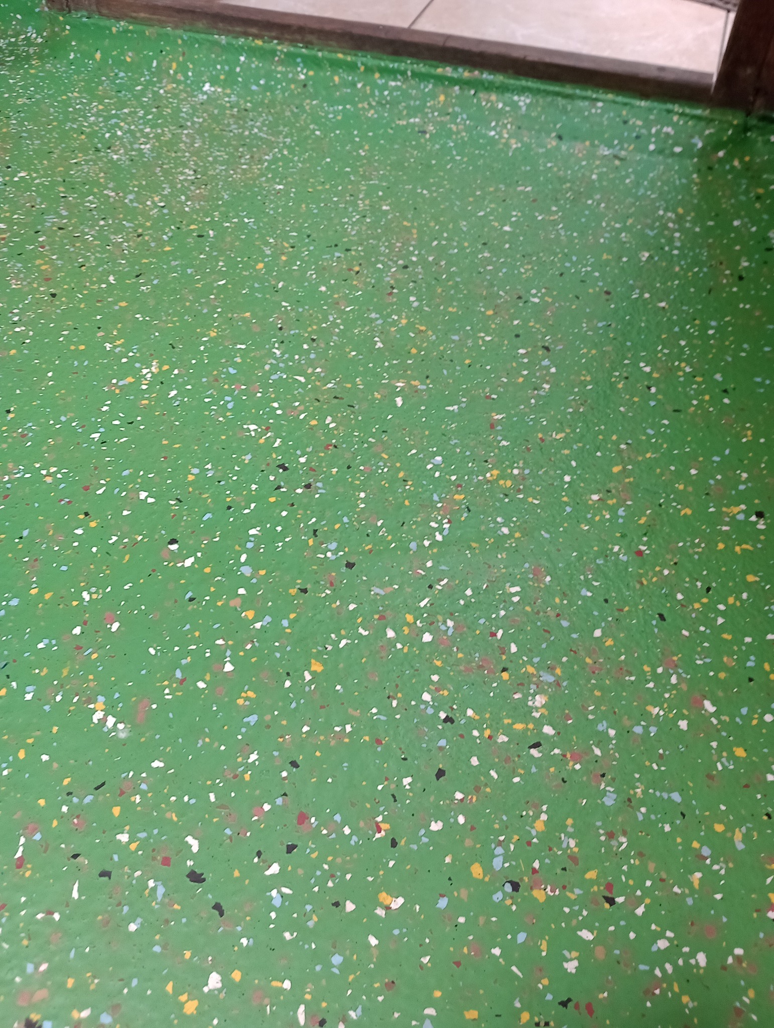 Zielona posadzka żywiczna z kolorowymi płatkami, widoczny fragment progu.