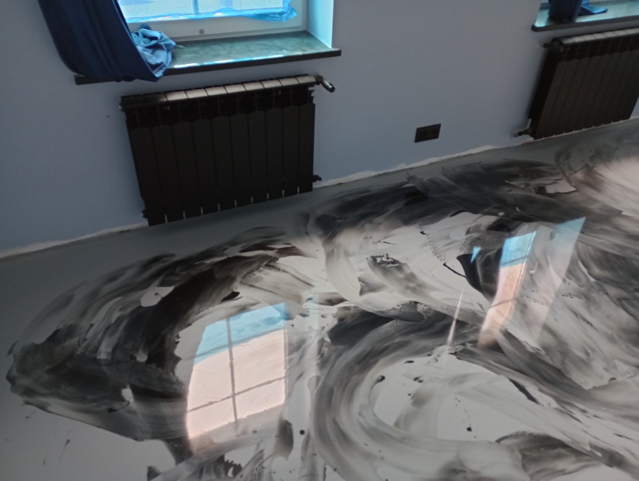 Biało-czarna podłoga z efektem marmuru w pomieszczeniu z grzejnikiem i oknem zasłoniętym niebieską tkaniną.