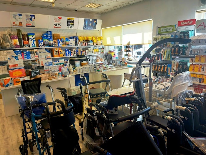 Wnętrze sklepu z artykułami rehabilitacyjnymi i pomocami dla osób starszych, w tym chodziki, wózki inwalidzkie i podnośniki, z półkami wypełnionymi produktami medycznymi w tle.