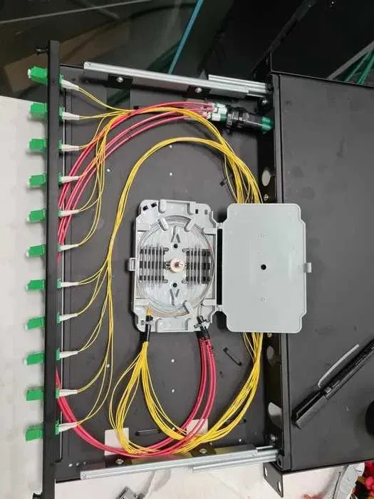 Rozdzielnica światłowodowa z widocznymi kablami w kolorach żółtym i czerwonym, podłączonymi do złączek z zielonymi elementami mocującymi.