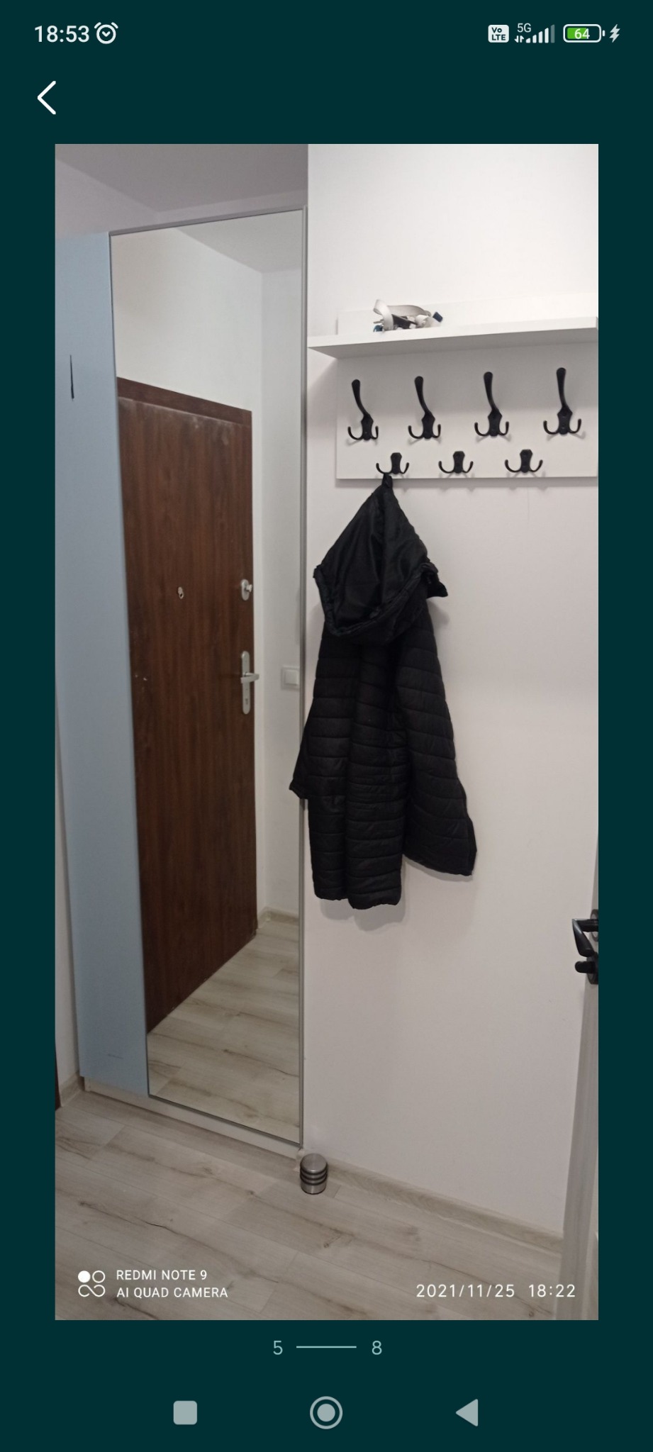 Przedpokój po remoncie: Lustro w zabudowie, wieszak z czarnymi haczykami i kurtką, widok na drzwi wejściowe odbijające się w lustrze.