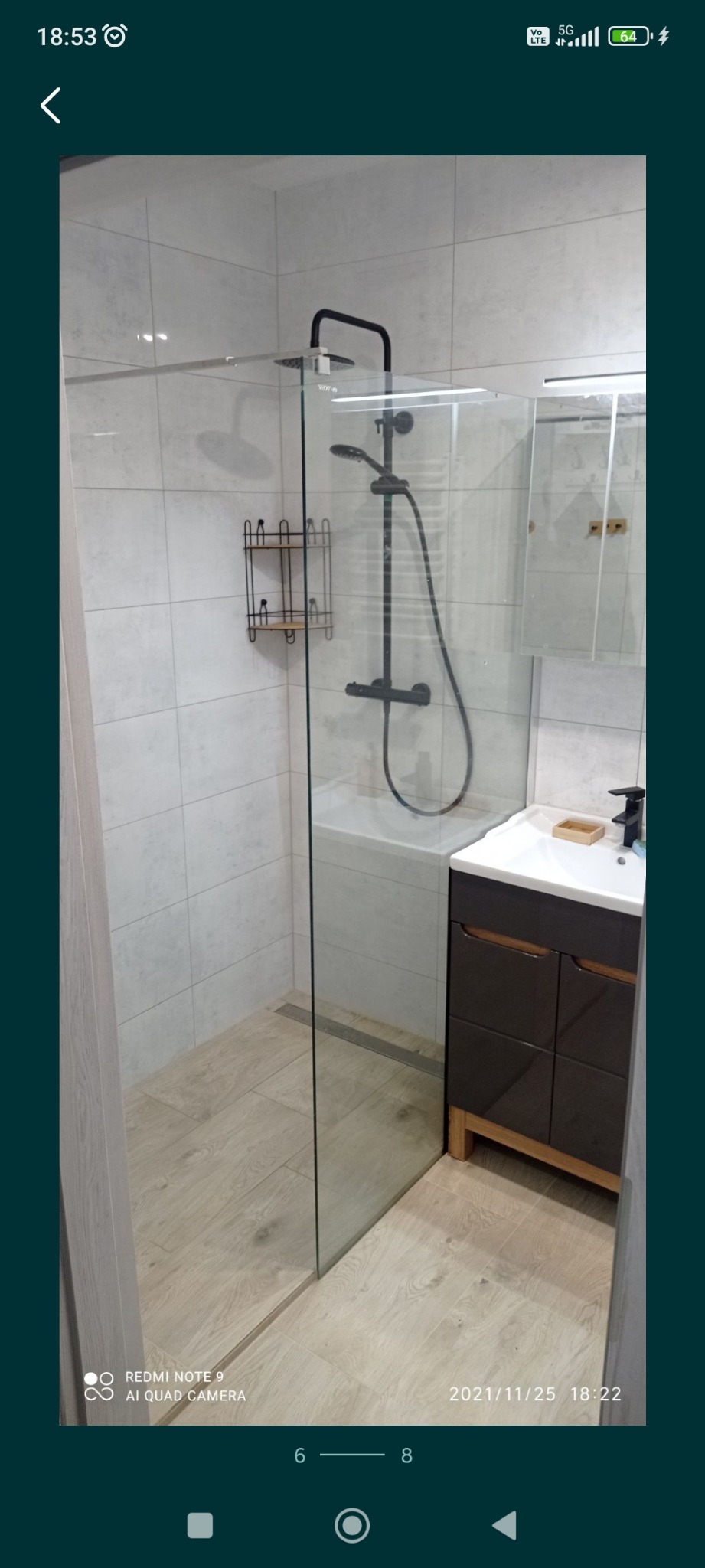 Nowoczesna kabina prysznicowa z czarną armaturą, szklaną ścianką i odpływem liniowym, widoczna umywalka z szafką w kolorze grafitowym.