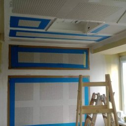 Zal - Bud - Przygotowania do prac wykończeniowych w pomieszczeniu biurowym: zabezpieczone taśmą perforowane panele ścienne i sufitowe, drewniana drabina w tle.