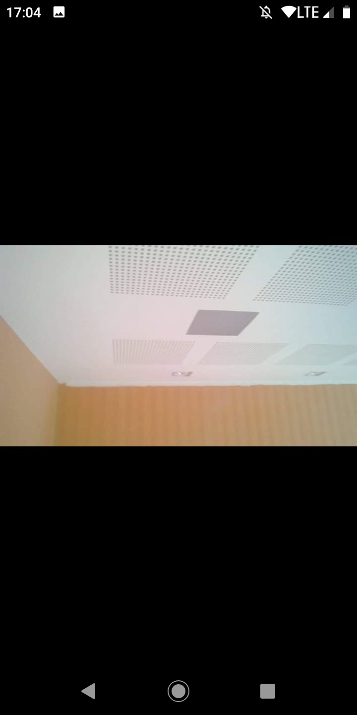 Sufit z perforowanymi panelami i jednym panelem rewizyjnym, widok z dołu na pomarańczową ścianę.