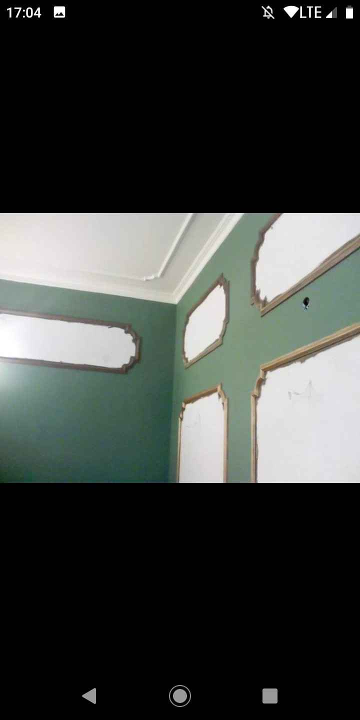 Zielona ściana z dekoracyjnymi, białymi panelami w trakcie montażu i wykończenia, widoczny fragment sufitu z listwą ozdobną.