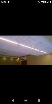 Sufit podwieszany z oświetleniem LED wzdłuż krawędzi, widok z dołu, ściany w ciepłym odcieniu beżu.