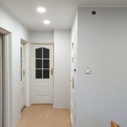 Grzegorz Tryc - Korytarz w domu jednorodzinnym we Wrocławiu po świeżym pomalowaniu ścian na szaro, widoczne trzy białe drzwi i panele na podłodze z drobnymi zabrudzeniami po pracach wykończeniowych.