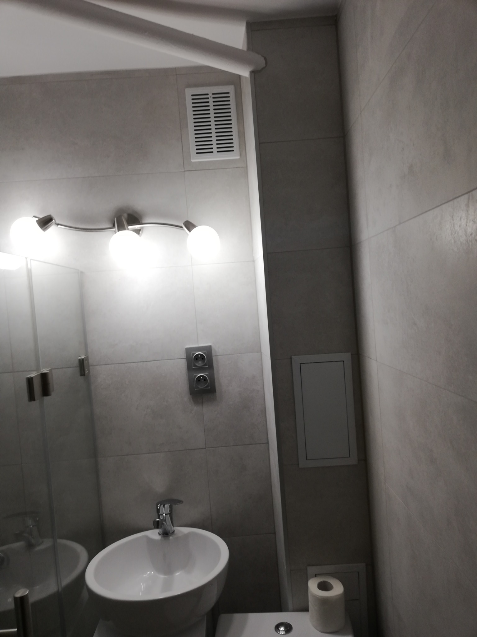 Nowoczesna łazienka z umywalką nablatową, szklaną kabiną prysznicową, jasnymi płytkami ściennymi i trzypunktową lampą sufitową.