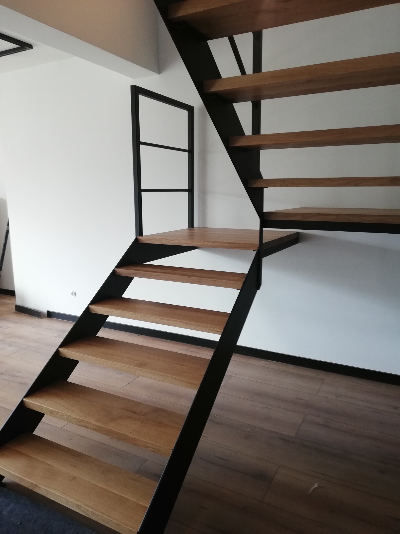 Schody drewniane z czarną, metalową konstrukcją w nowoczesnym wnętrzu, widok z dołu na stopnie i minimalistyczną balustradę