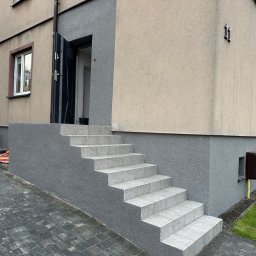 RavBud usługi ogólnobudowlane - Wykończone płytkami schody wejściowe do domu w Katowicach, z szarą elewacją i widocznym fragmentem chodnika z kostki brukowej.