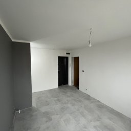 RavBud usługi ogólnobudowlane - Wnętrze po remoncie z szarą ścianą akcentującą, szarą podłogą z płytek i surową żarówką zwisającą z sufitu.